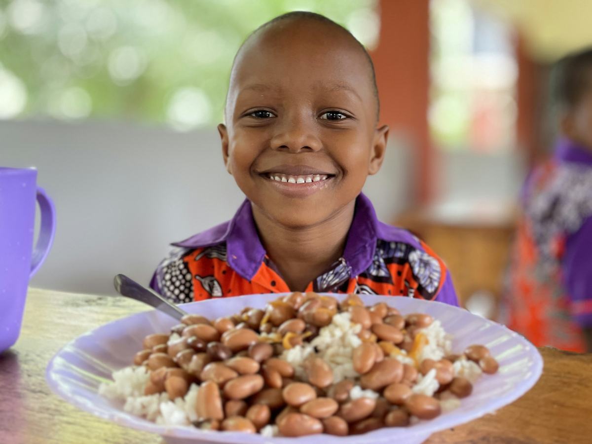 A smiling boy with a plate of rice and beans in Kenya