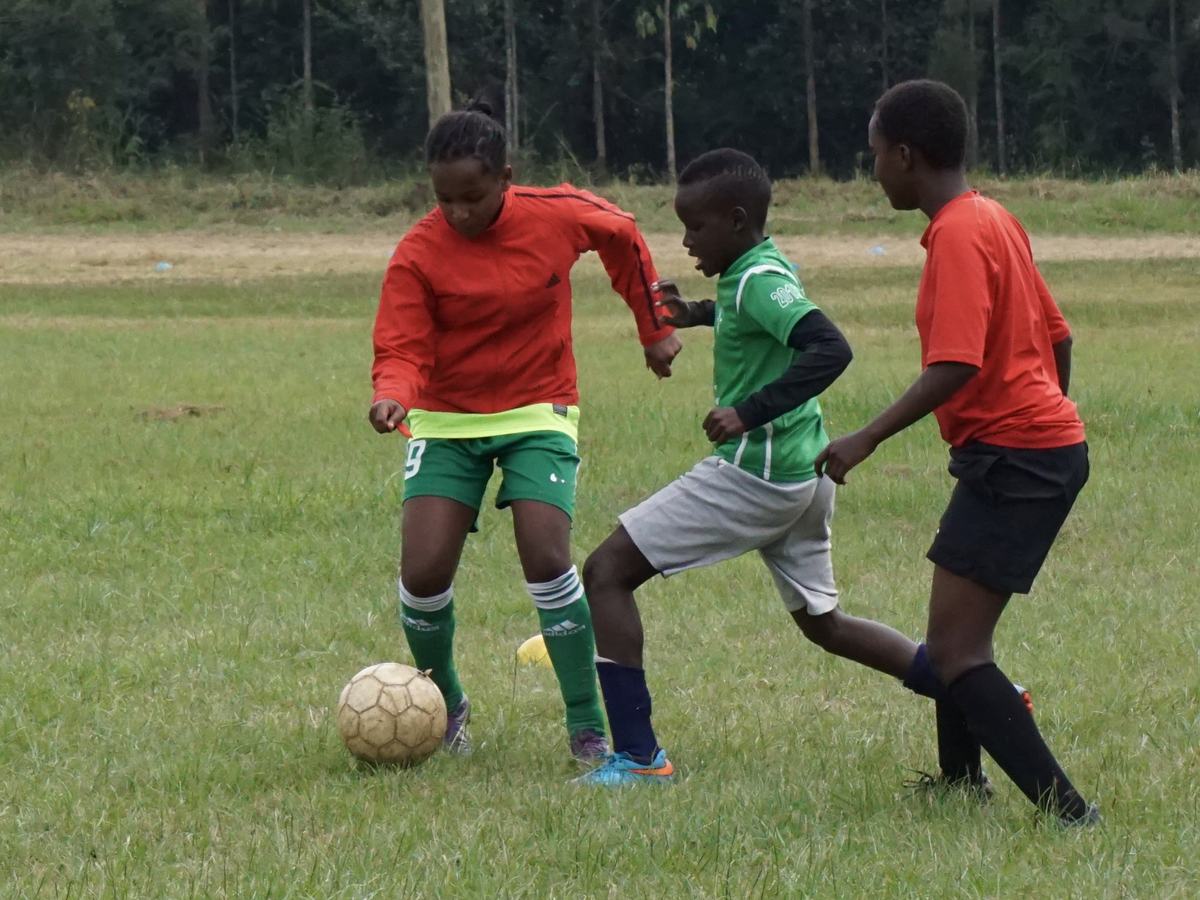A girl dribbling a football past two boys in Kenya